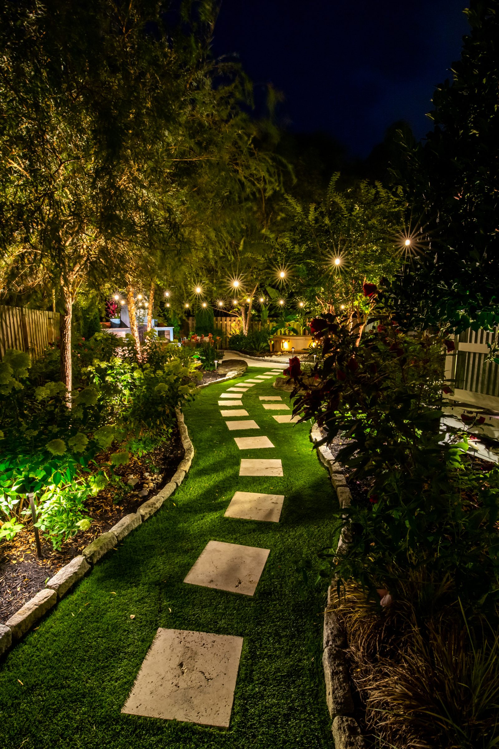 Brass landscape lighting fixtures lighting a home and plantings in the evening